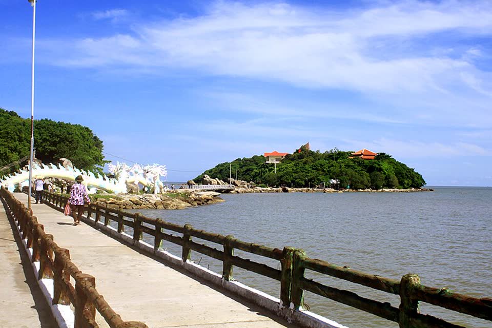 A concrete walkway leading to the tree-covered islet at Hon Da Bac, with the sea on the right