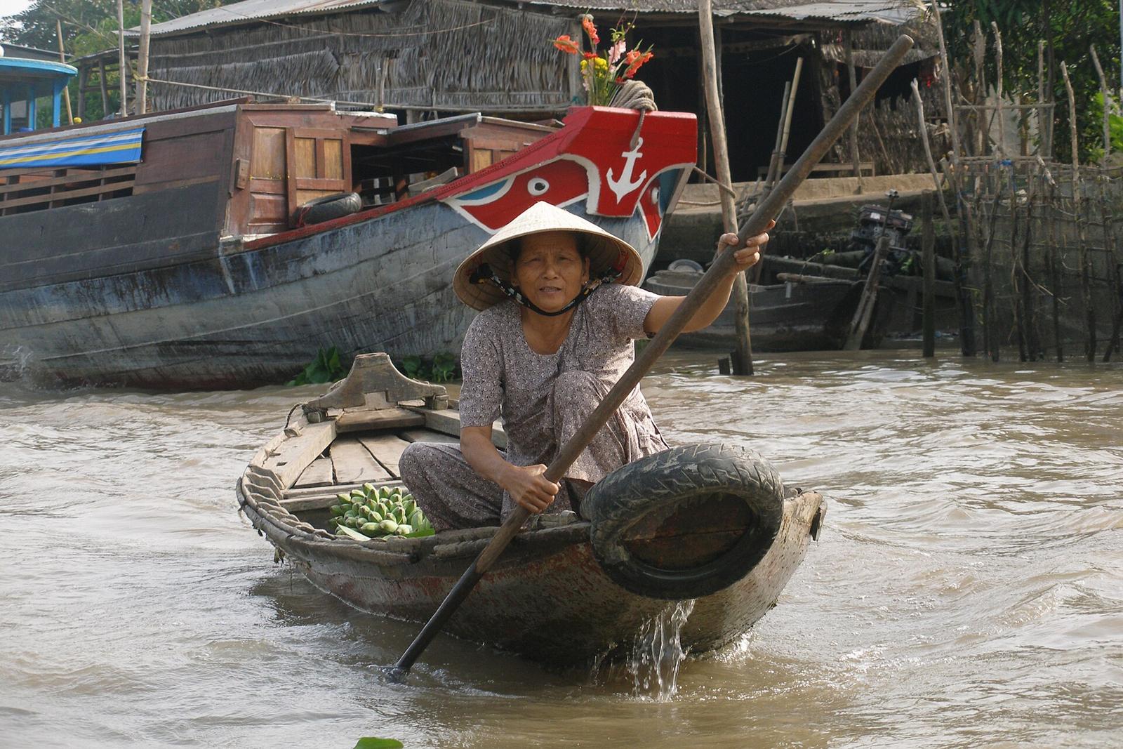 A woman in a conical hat rowing a small boat of vegetables at the Phong Dien floating market