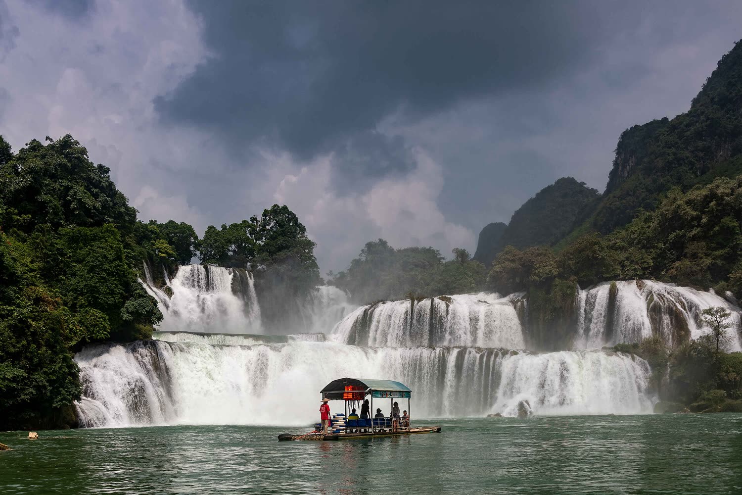 A covered bamboo raft on the Quay Son with Ban Gioc waterfall and limestone behind it