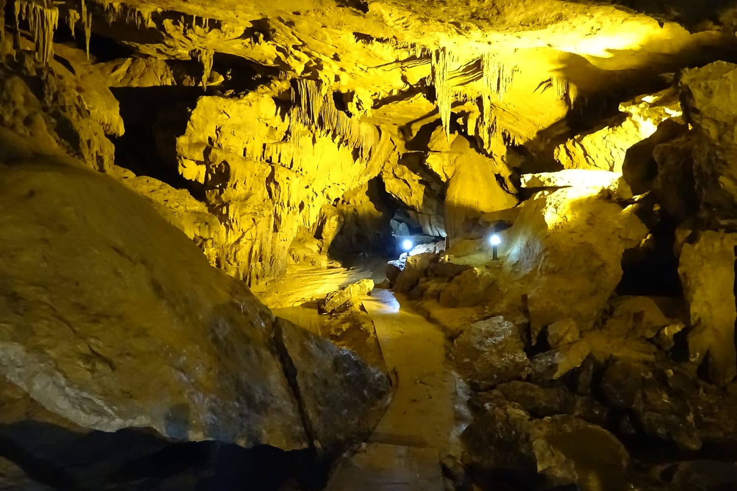 A path through a yellow-lit chamber of Nguom Ngao cave, with stalactites overhead