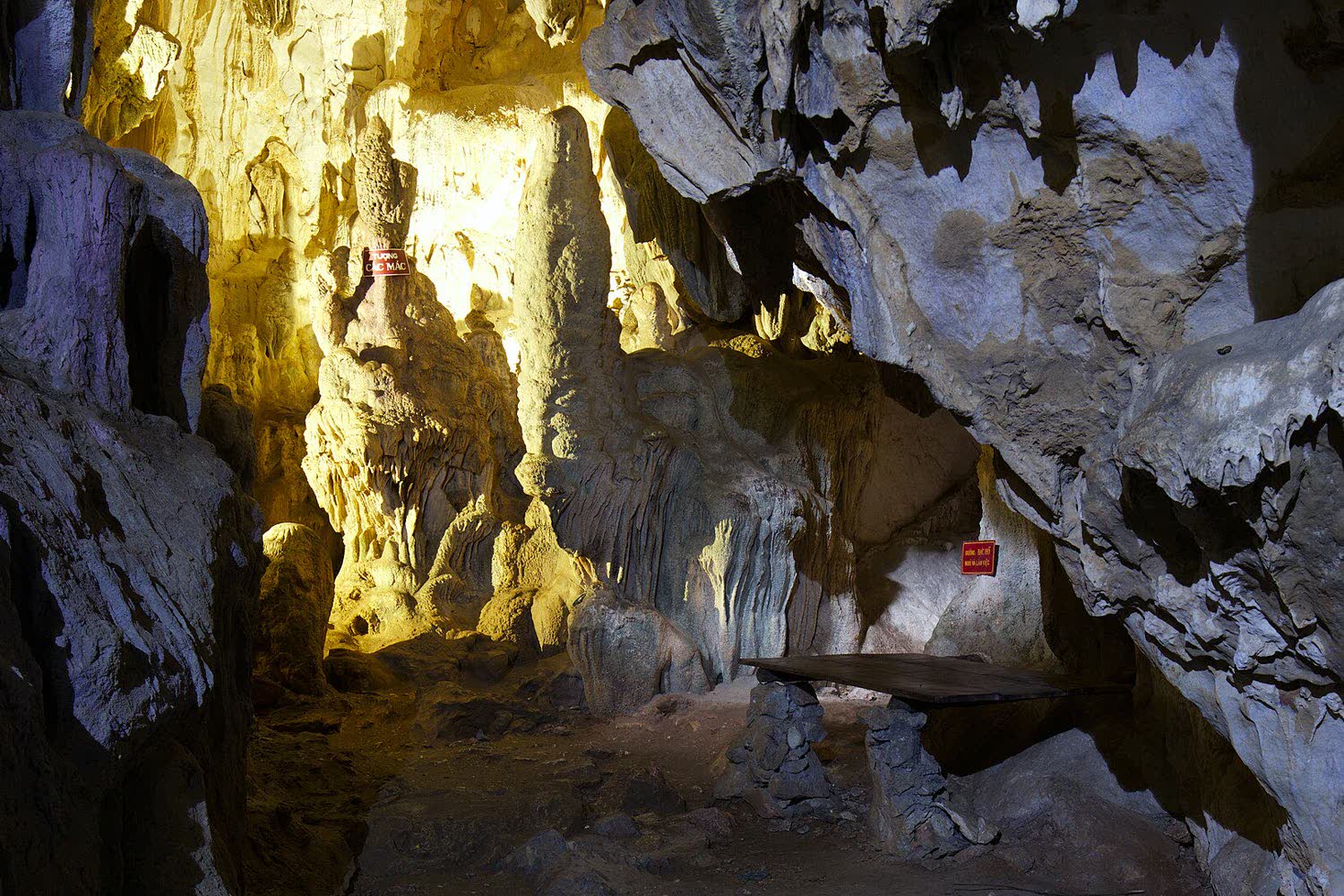 The lit interior of Coc Bo cave, with stalactites and a wooden table