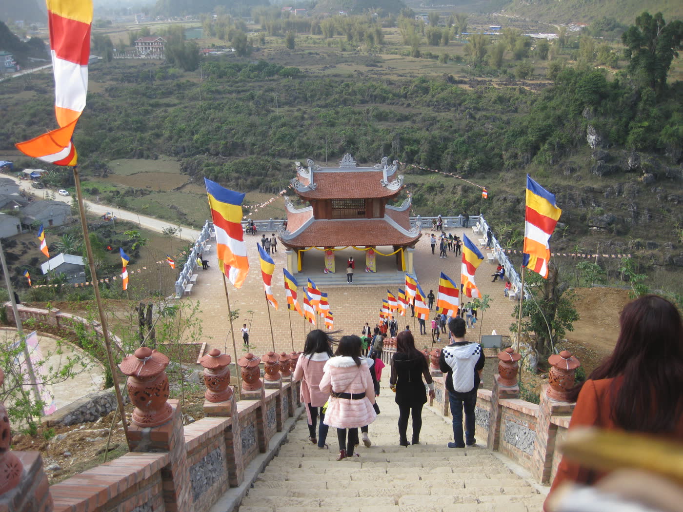 People walking down stone stairs toward the tiled gate hall at Truc Lam Ban Gioc, with the valley behind