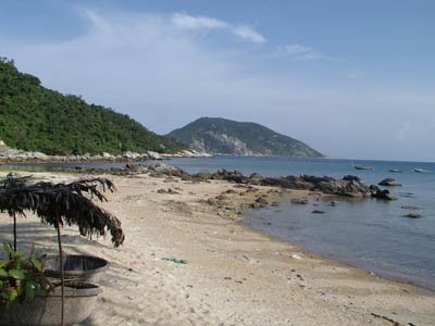 A sandy beach at Bai Huong with rocks, clear water, and a forested island across the bay