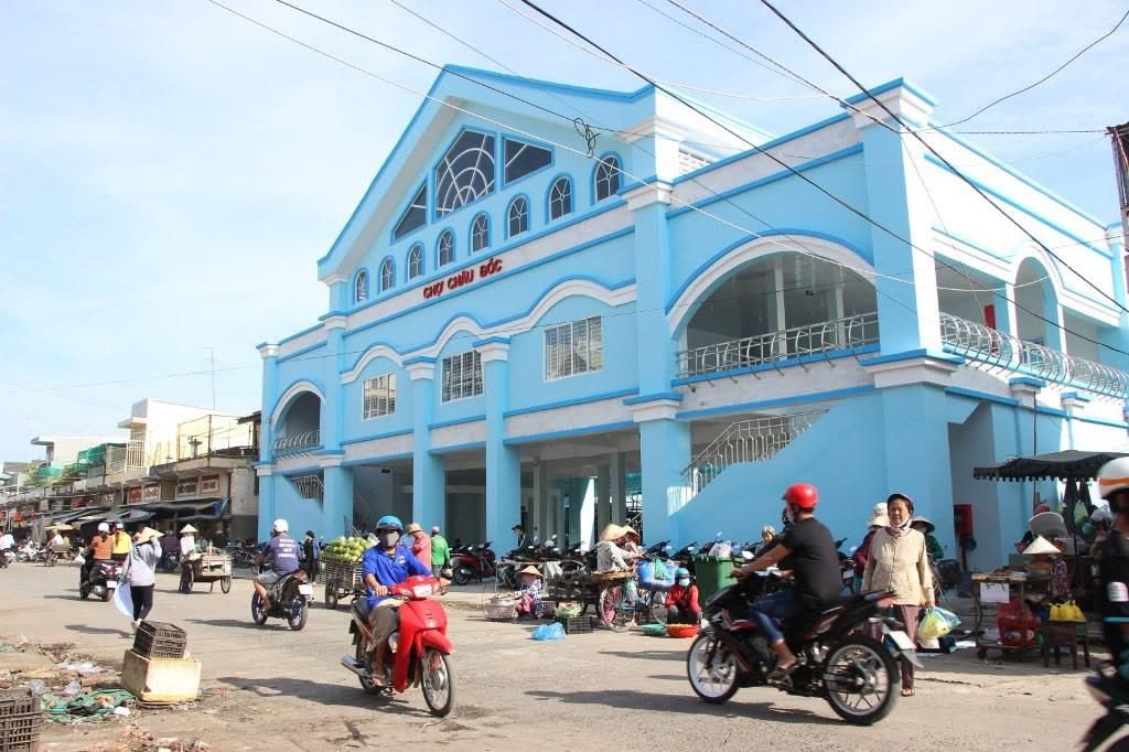The blue Chau Doc Market building with motorbikes and produce on the street