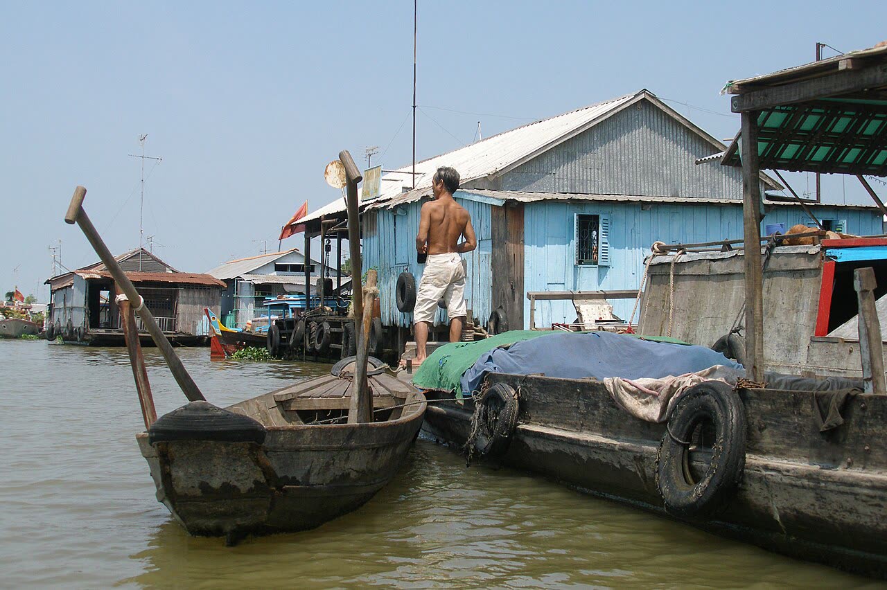 A man standing on a fish-farm raft with wooden boats alongside at Chau Doc