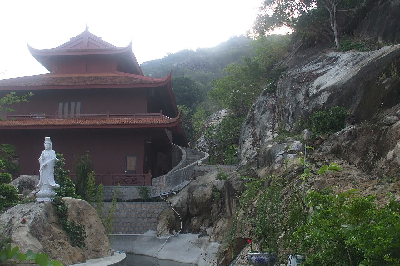 Cave Pagoda built into the rock of Sam Mountain, with a white statue in front
