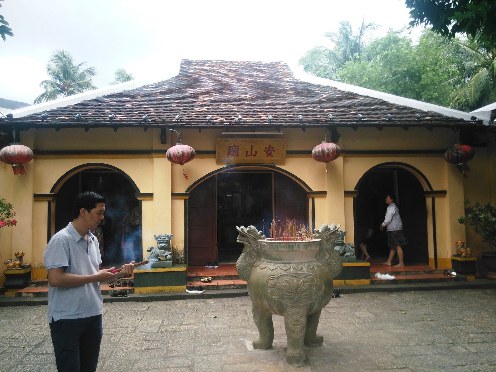 A bronze incense burner in front of the yellow hall of An Son temple, with red lanterns
