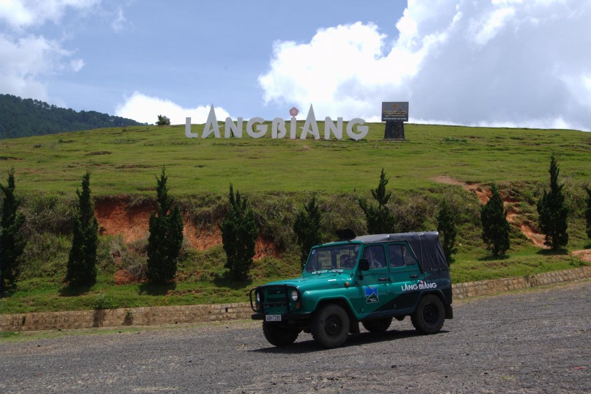 Green tourist jeep on the road below the Langbiang sign on a grassy hill