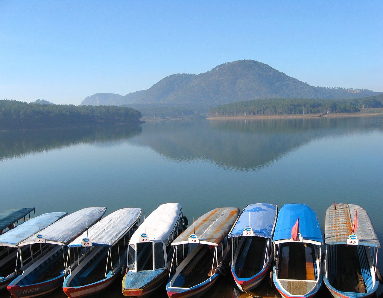 Covered boats lined up on Tuyen Lam Lake, hills across the water