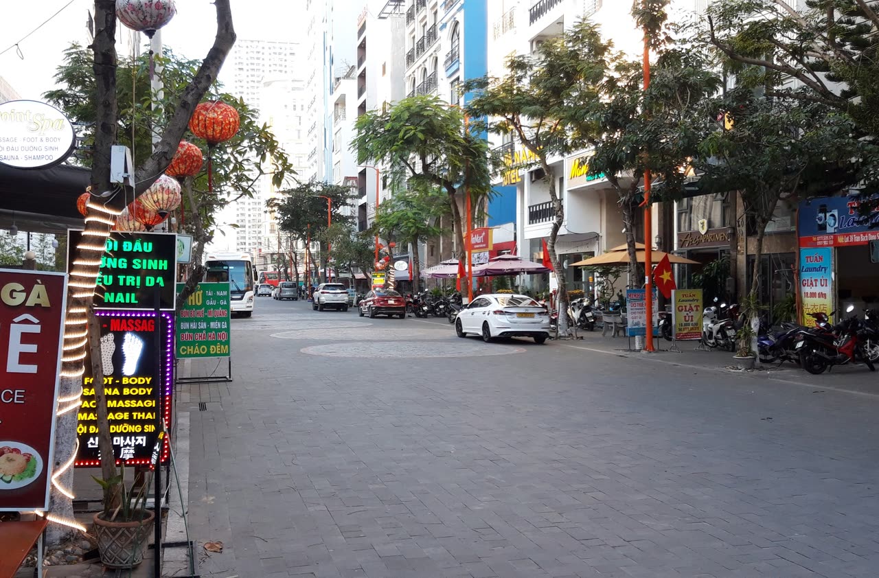 A paved street inside the An Thuong quarter with red lanterns, lit spa boards, parked motorbikes, and hotel fronts