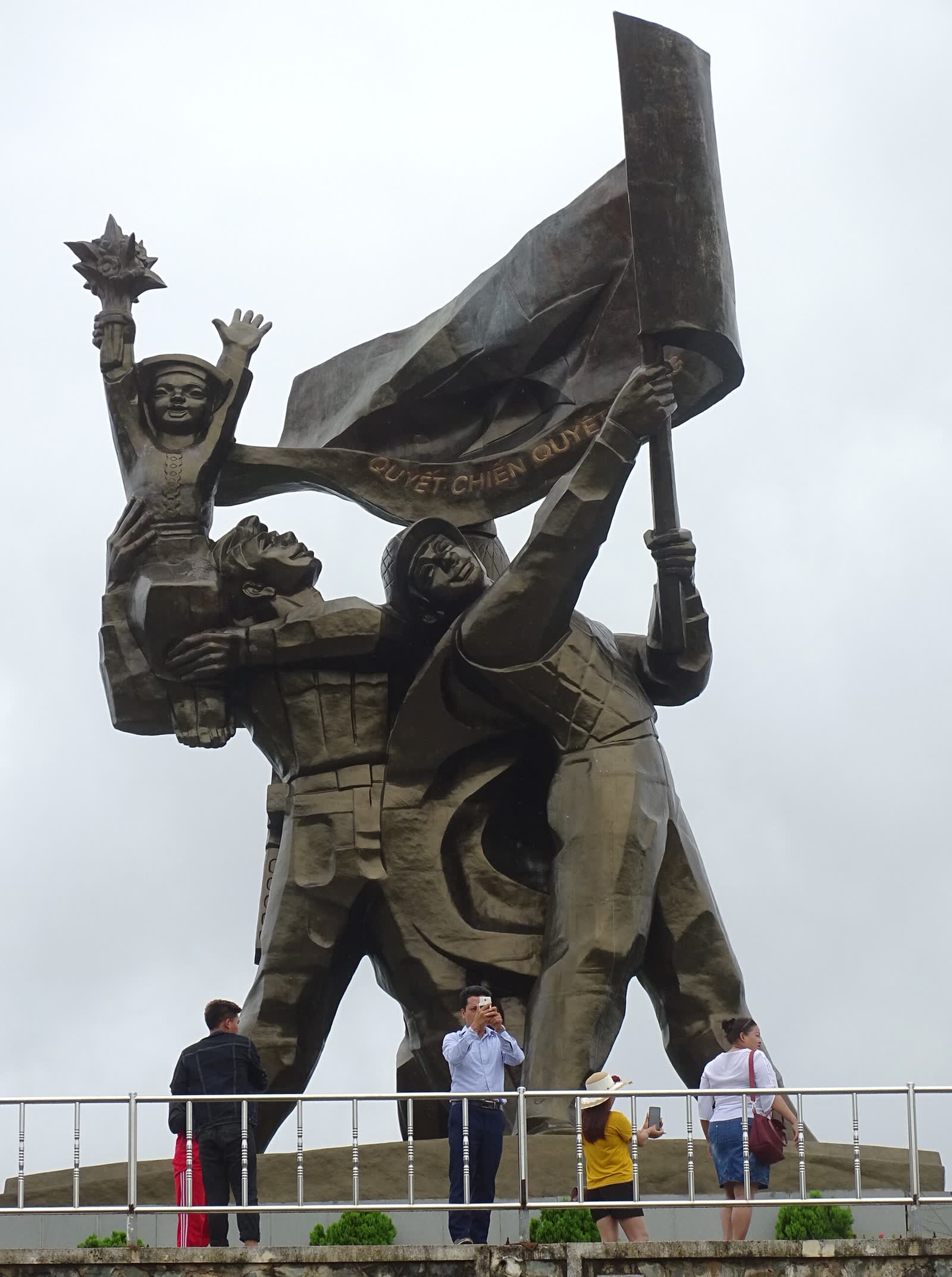 Visitors looking up at the copper victory group and the flag on Hill D1 in Dien Bien Phu