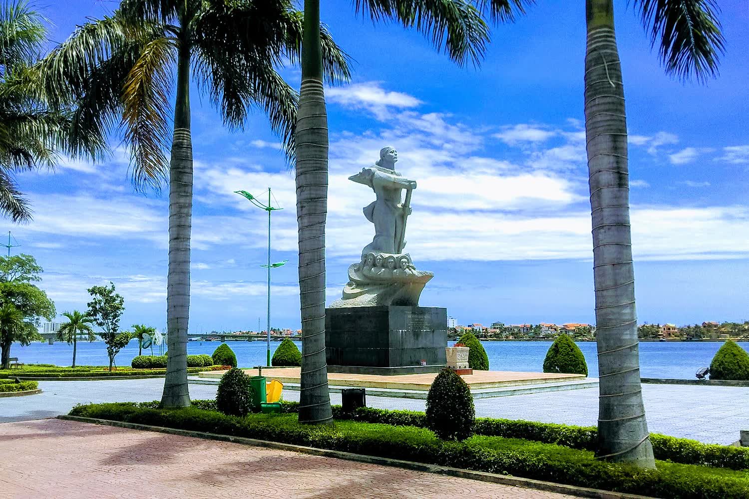 The Mother Suốt statue among palms, with the Nhật Lệ behind