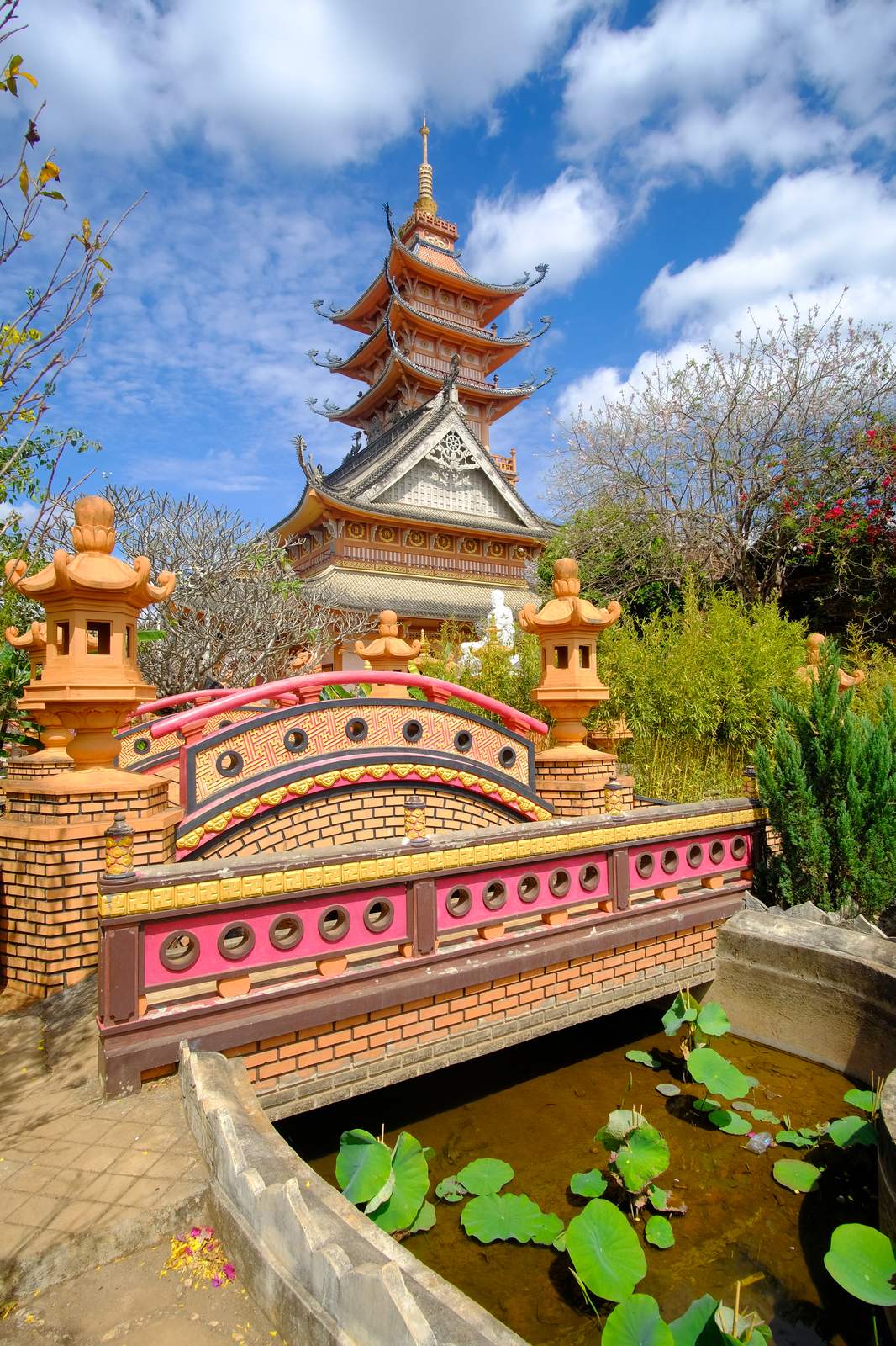 Multi-tier tower of Buu Minh Pagoda behind a brick garden bridge and a lotus pond