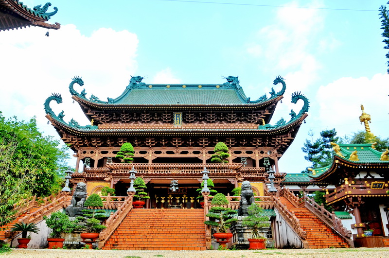 Wooden hall of Minh Thanh Pagoda with a tiled roof, guardian lions, and a brick stair