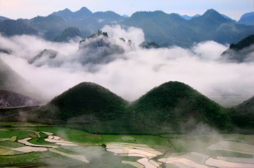 Two rounded hills at Quản Bạ rising through cloud above rice terraces