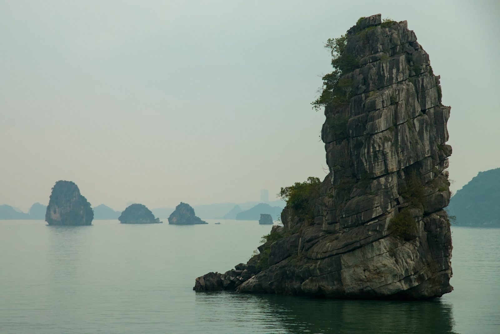 A tall limestone rock in Bai Tu Long Bay, with more islands on the horizon