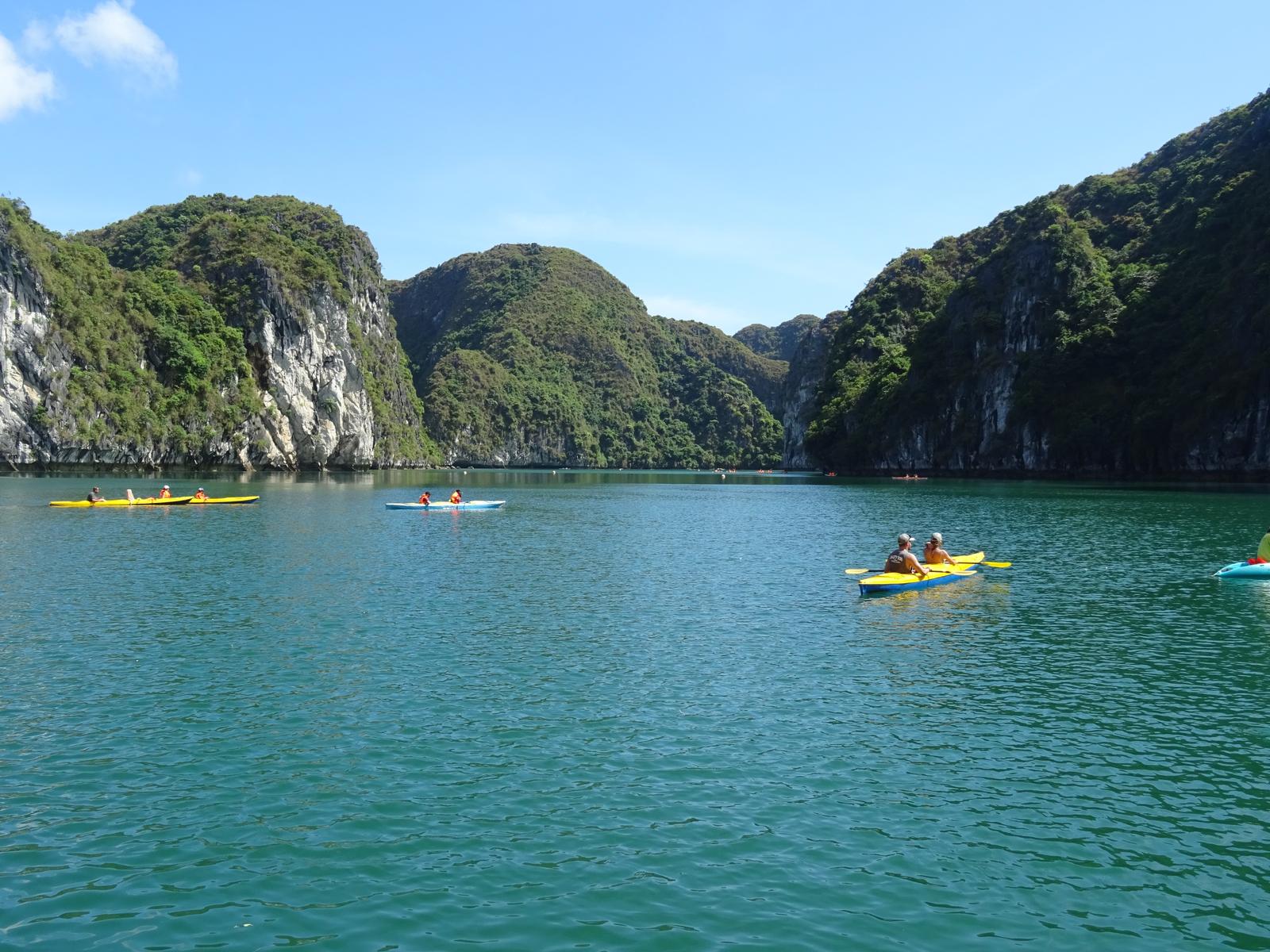 Several kayaks on a calm lagoon in Ha Long Bay, limestone hills around them