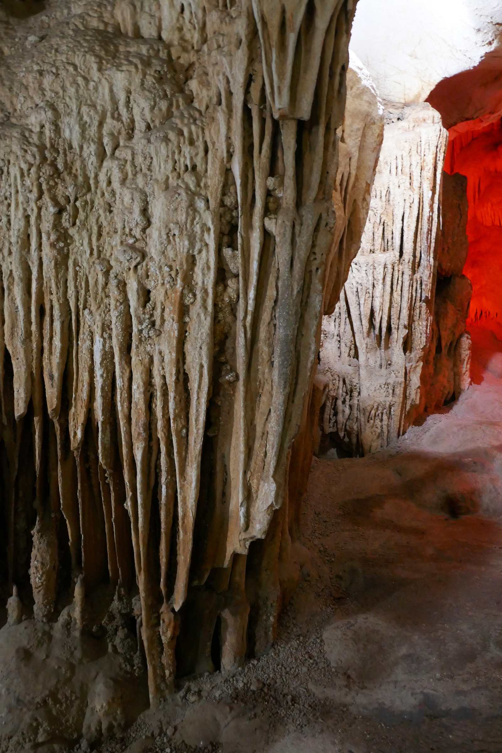 Limestone formations inside Me Cung Cave, Ha Long Bay, with a red-lit chamber behind