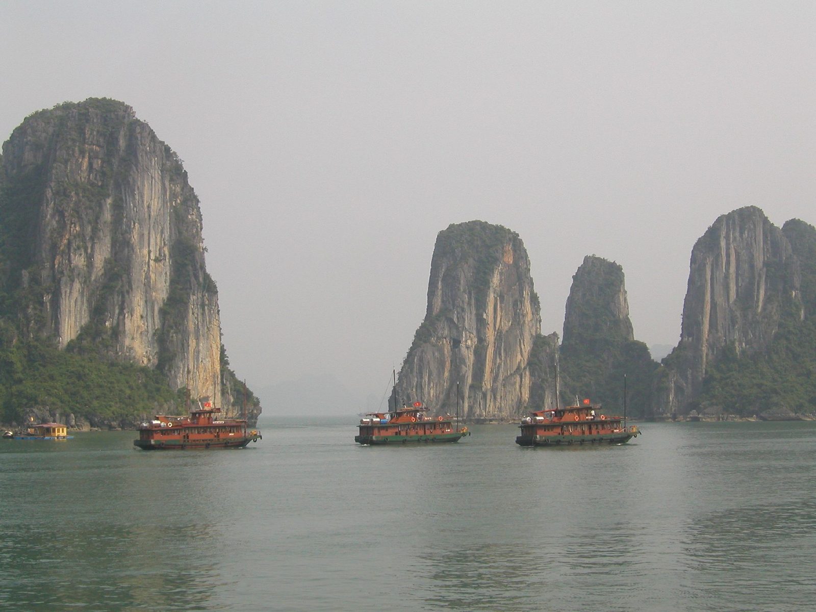 Three wooden cruise boats on Ha Long Bay with limestone towers behind them