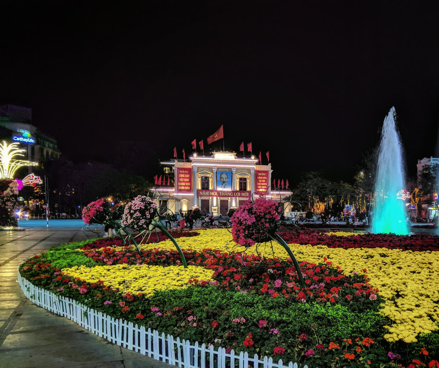The Hai Phong opera house lit at night, with flower beds and a fountain in the square