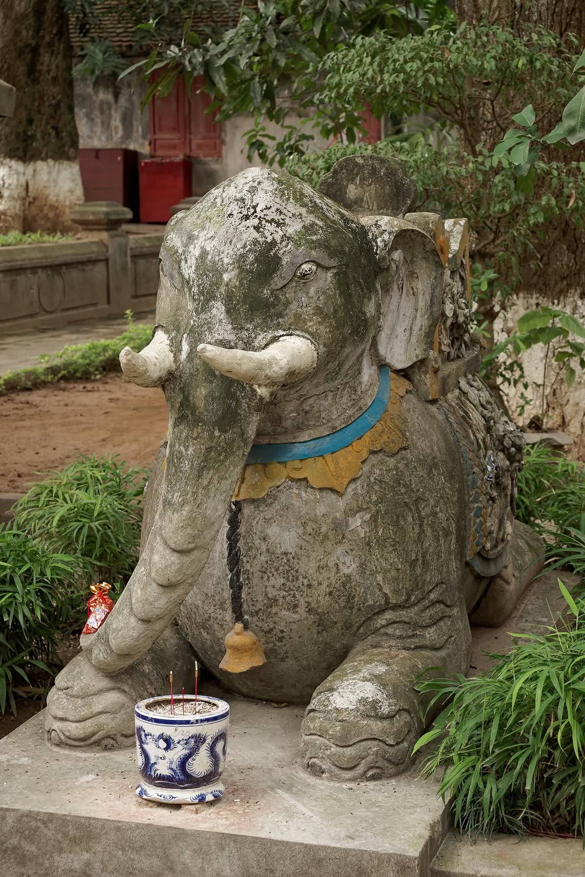A stone elephant with a blue and gold harness in the courtyard of Quan Thanh Temple
