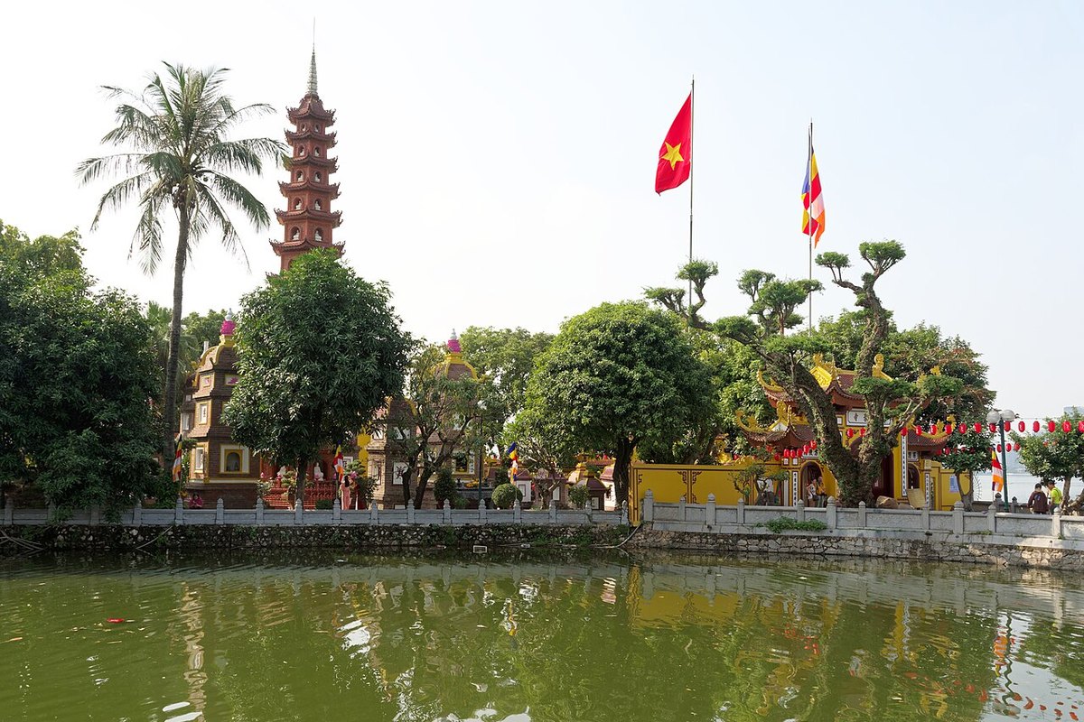 Tran Quoc Pagoda's red stupa behind trees and flags, seen across the water of West Lake