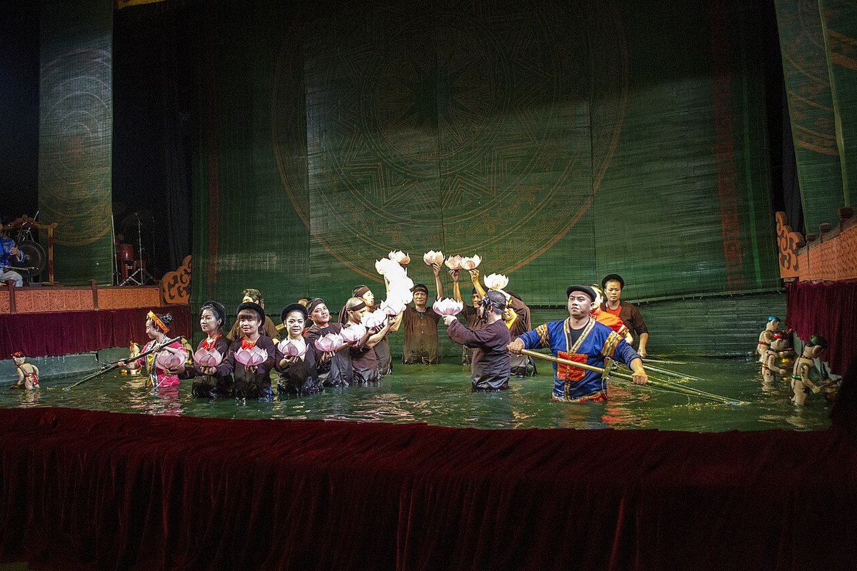 Water puppeteers in costume standing in the pool in front of the stage curtain at the Thang Long Water Puppet Theatre