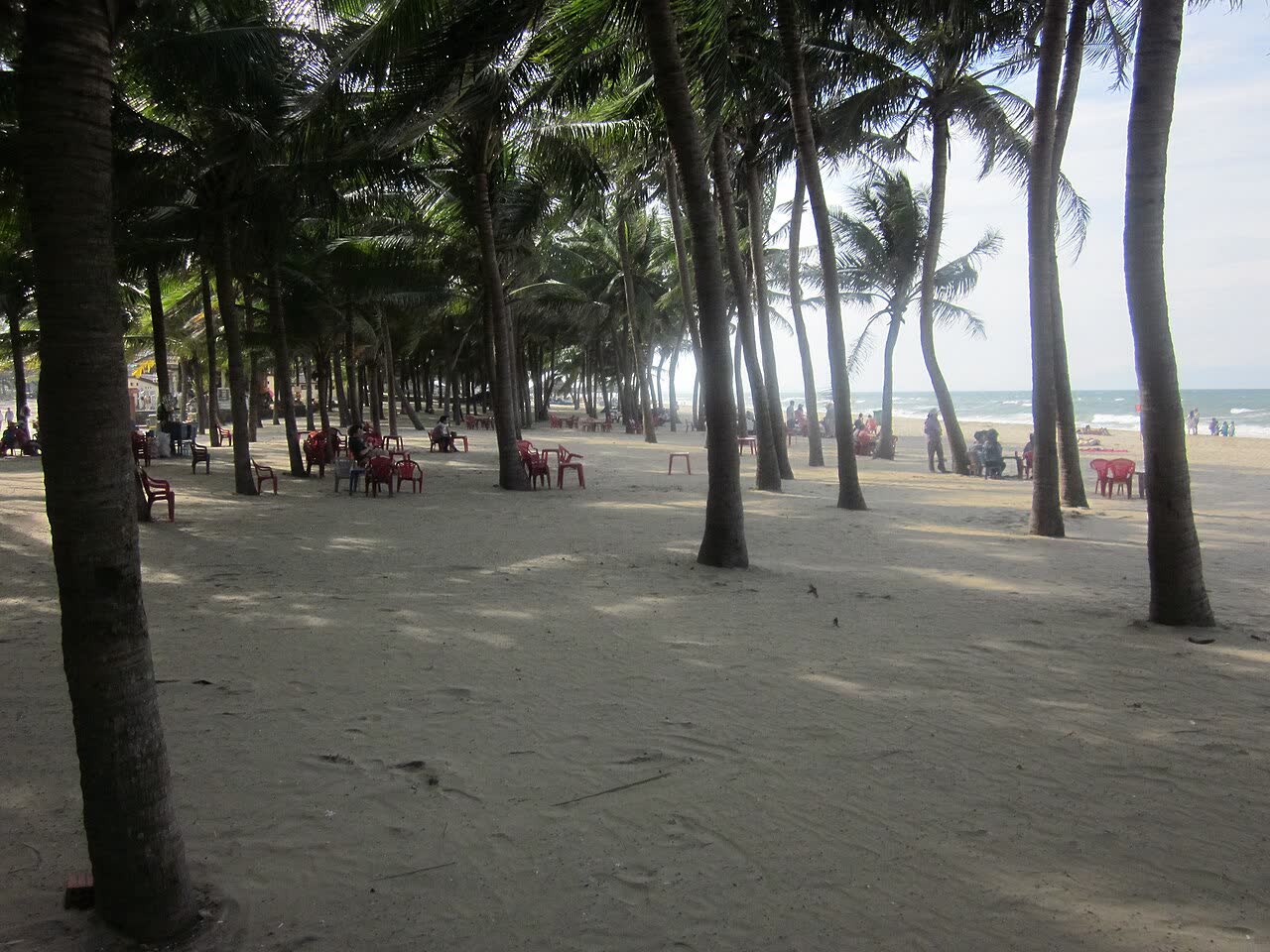 Palm shade and people on the sand at Canh Duong beach, with the sea beyond