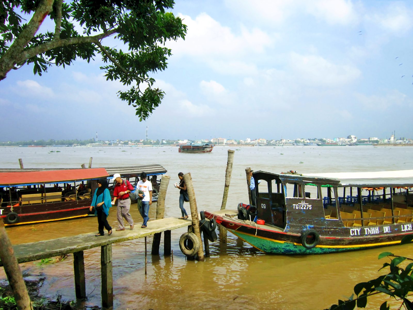 Wooden tour boats tied at a landing on Thoi Son, with the river and the far bank