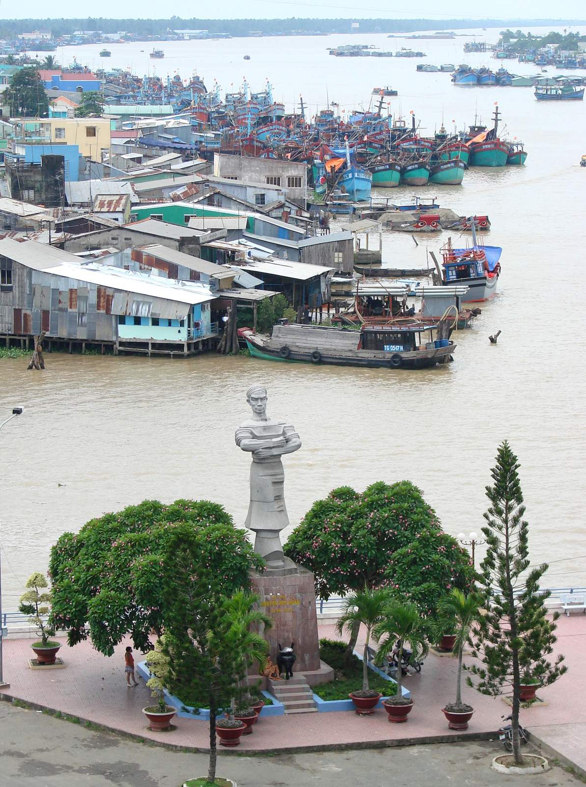 The Thủ Khoa Huân statue above the garden, with boats on the river behind the trees