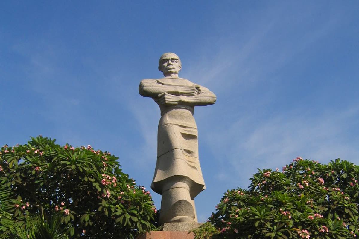 The statue above the garden trees, face and crossed arms in frame
