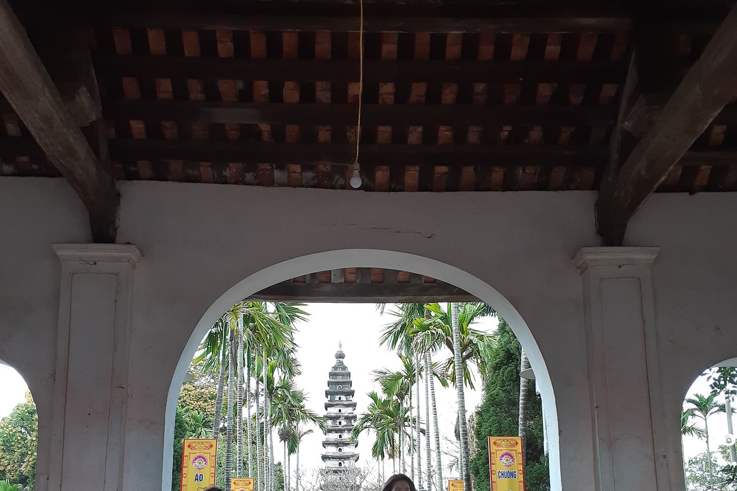 Pho Minh stone tower seen through an arched gate, with yellow festival banners and palms