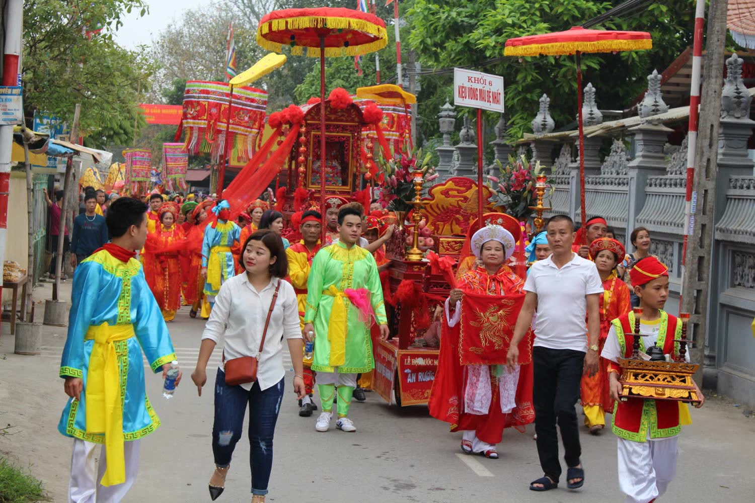 A festival procession with a red palanquin, umbrellas, and people in ceremonial dress