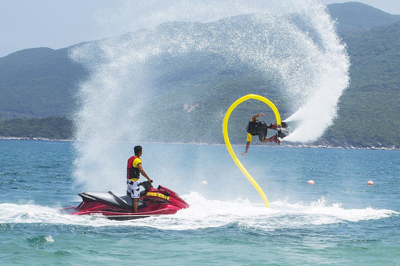 A person on a flyboard beside a red jet ski in the water at Hòn Tằm