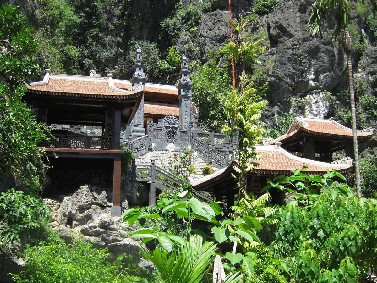 Carved wooden temple halls built against a limestone cliff at Am Tien
