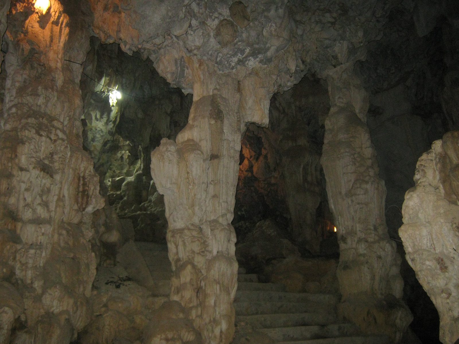 Lit limestone columns and a stone stair inside Dich Long cave