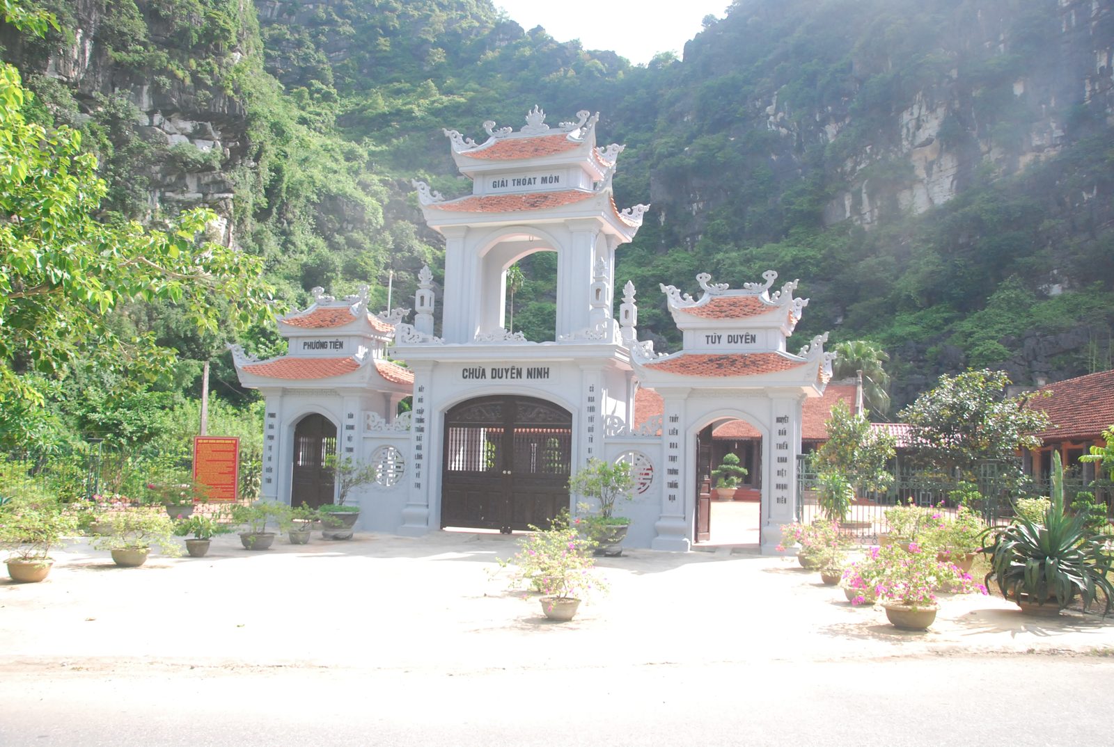 The white three-door gate of Duyen Ninh Pagoda against a limestone cliff