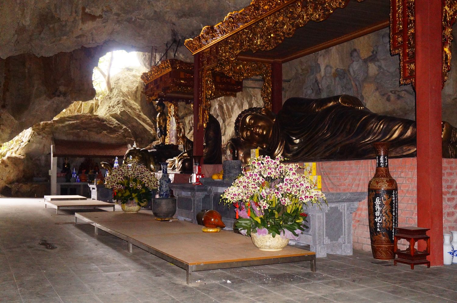 A dark bronze reclining Buddha in the cave of Ky Lan Pagoda, with daylight at the mouth
