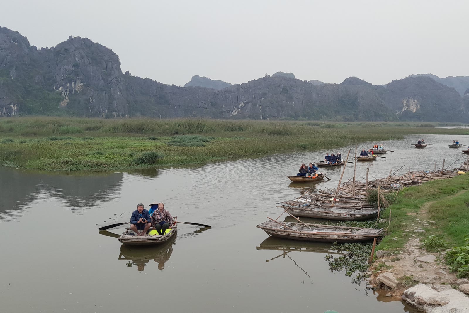 Wooden boats on a wetland channel with limestone hills at Vân Long
