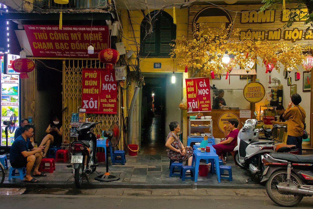 A shopfront signed for silver engraving at 100 Hàng Bạc, with people on plastic stools outside