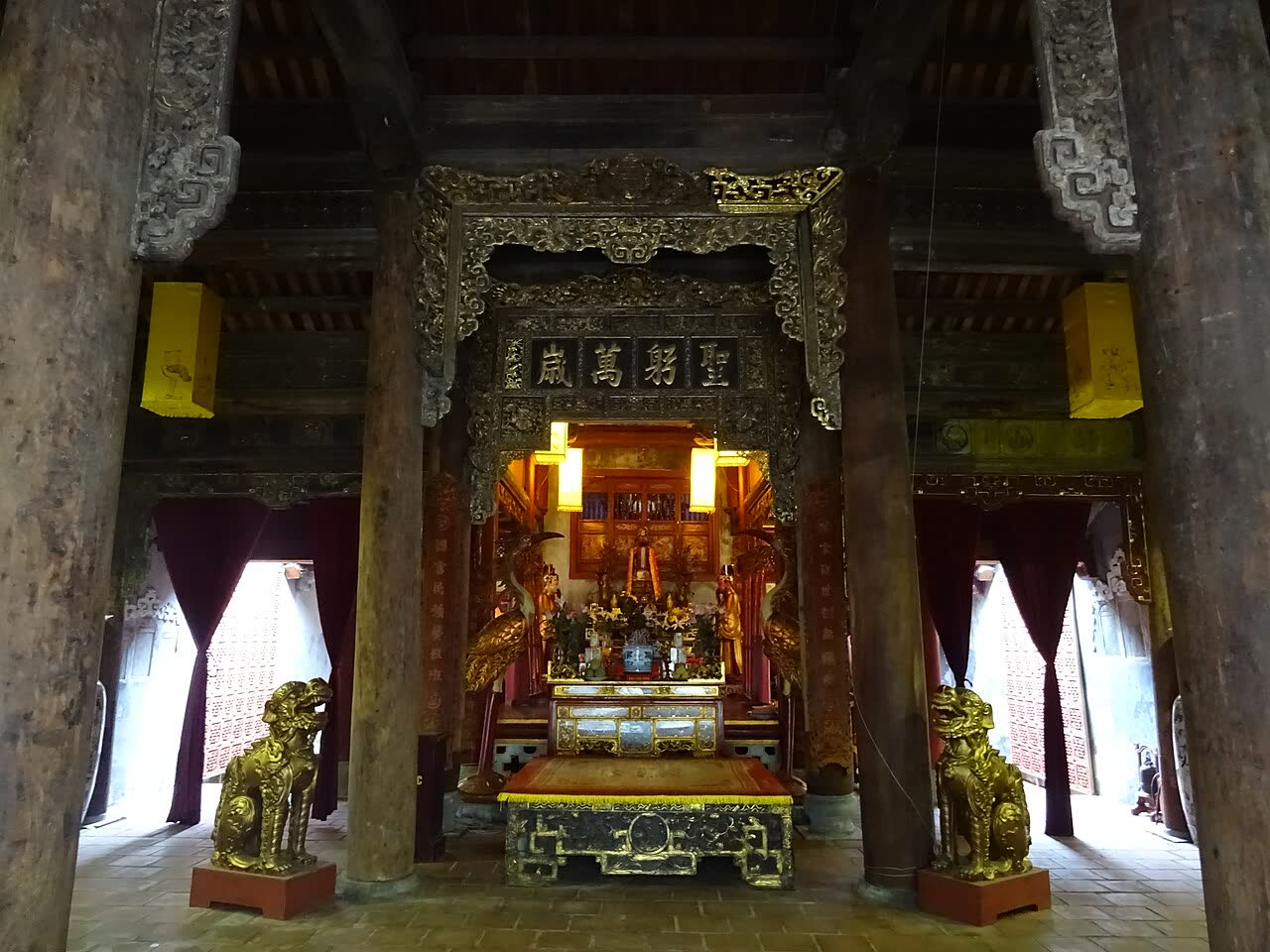 The carved wooden altar inside Kim Ngan Communal House, with gilded lions and incense
