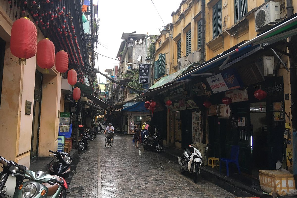 A narrow Old Quarter street in daylight, red lanterns on the left and bars with shutters on the right