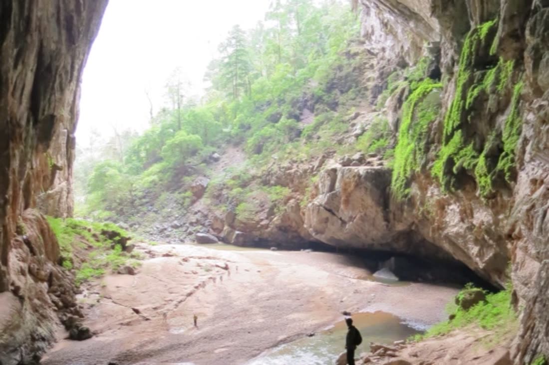 A sandy floor and a stream inside a large cave opening at Son Doong