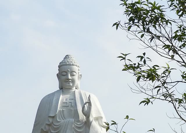 White standing Buddha at Thien An, face and raised hand, with leaves at the right
