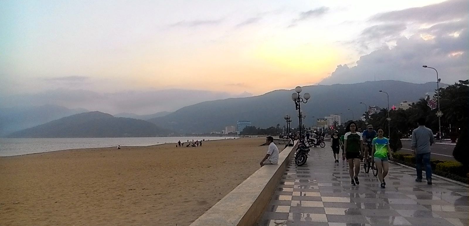 People walking the promenade beside the yellow sand of Quy Nhon beach at dusk