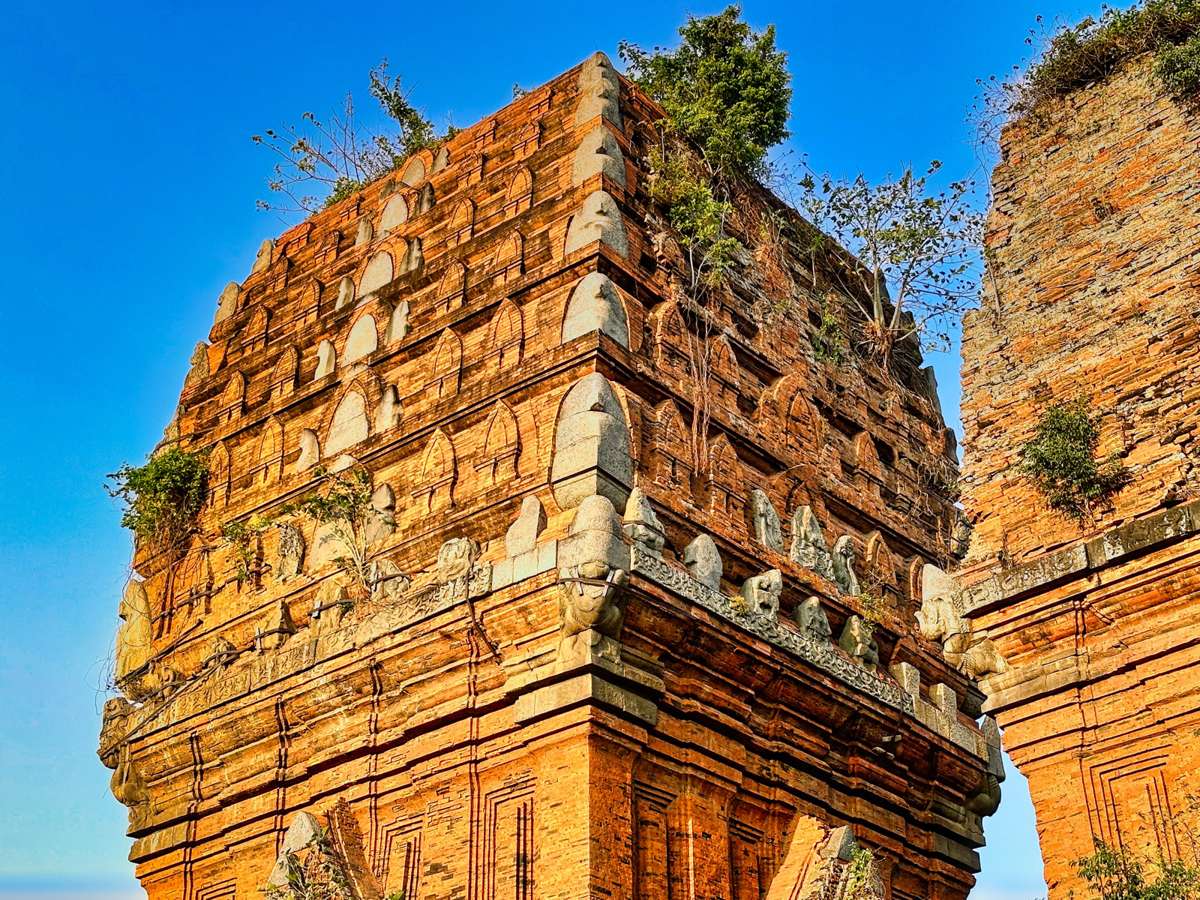 Brick corner of Tháp Đôi with carved figures under a blue sky