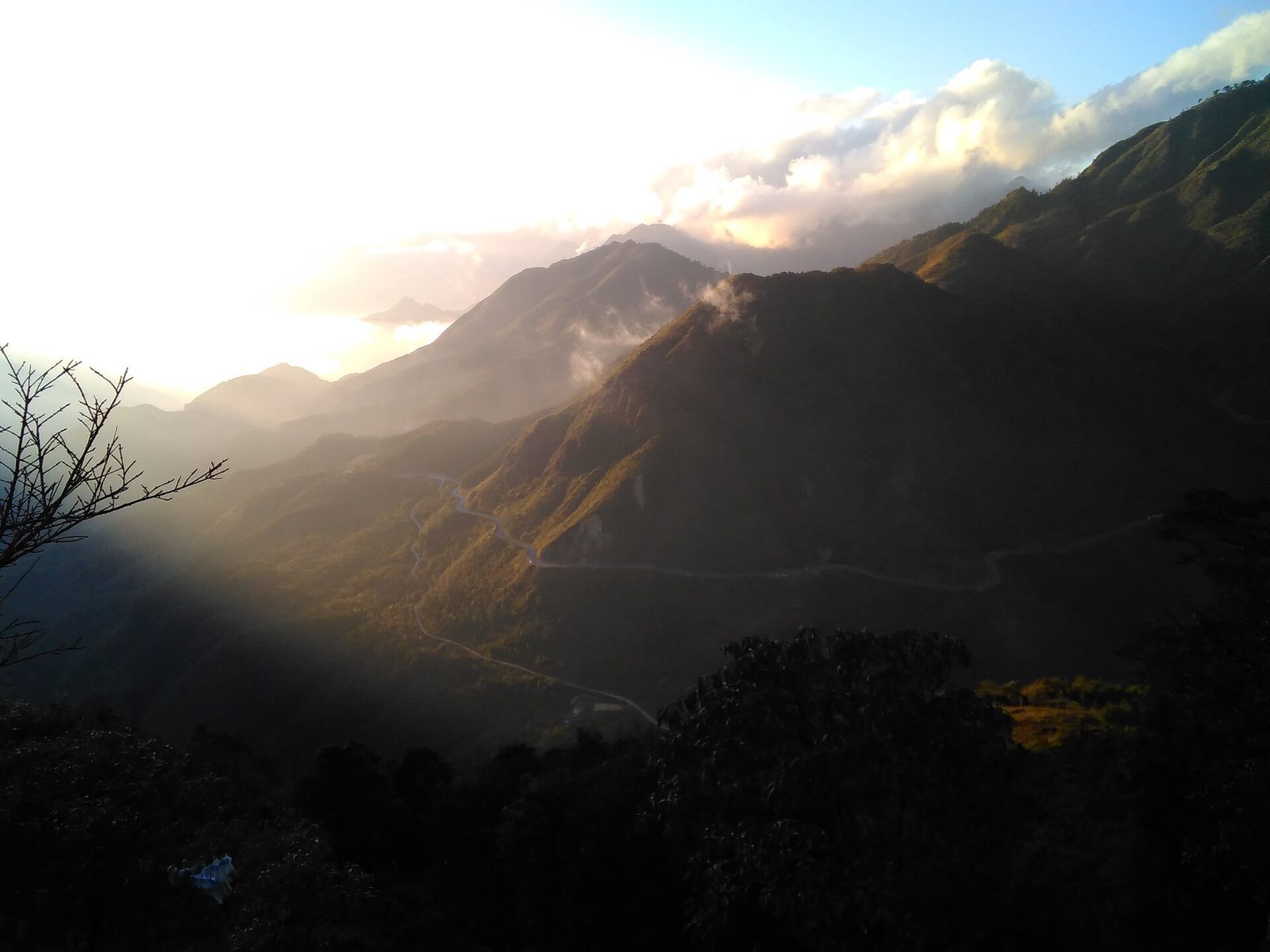 Winding road of O Quy Ho pass in low sun, with forested ridges