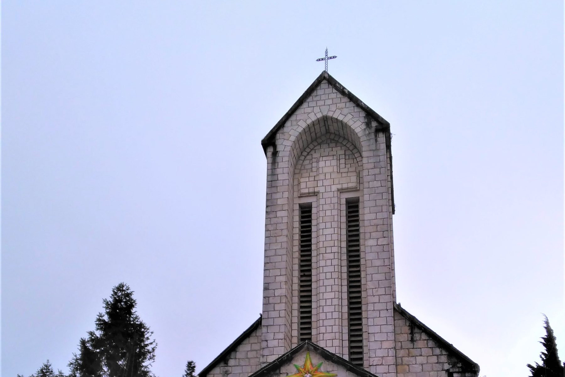 The stone tower and cross of the Sa Pa church against a pale sky