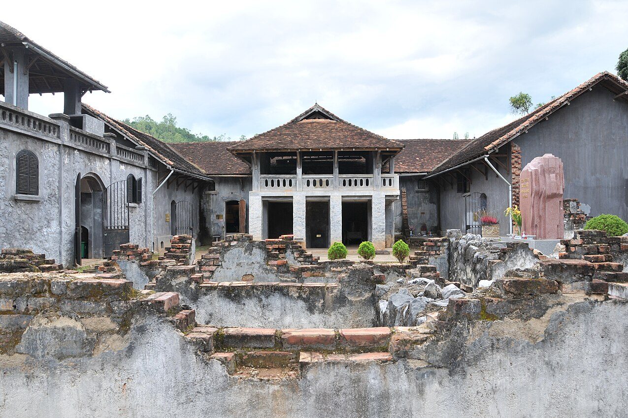 The courtyard of Son La Prison, with a tiled pavilion and a stone monument among the ruined walls