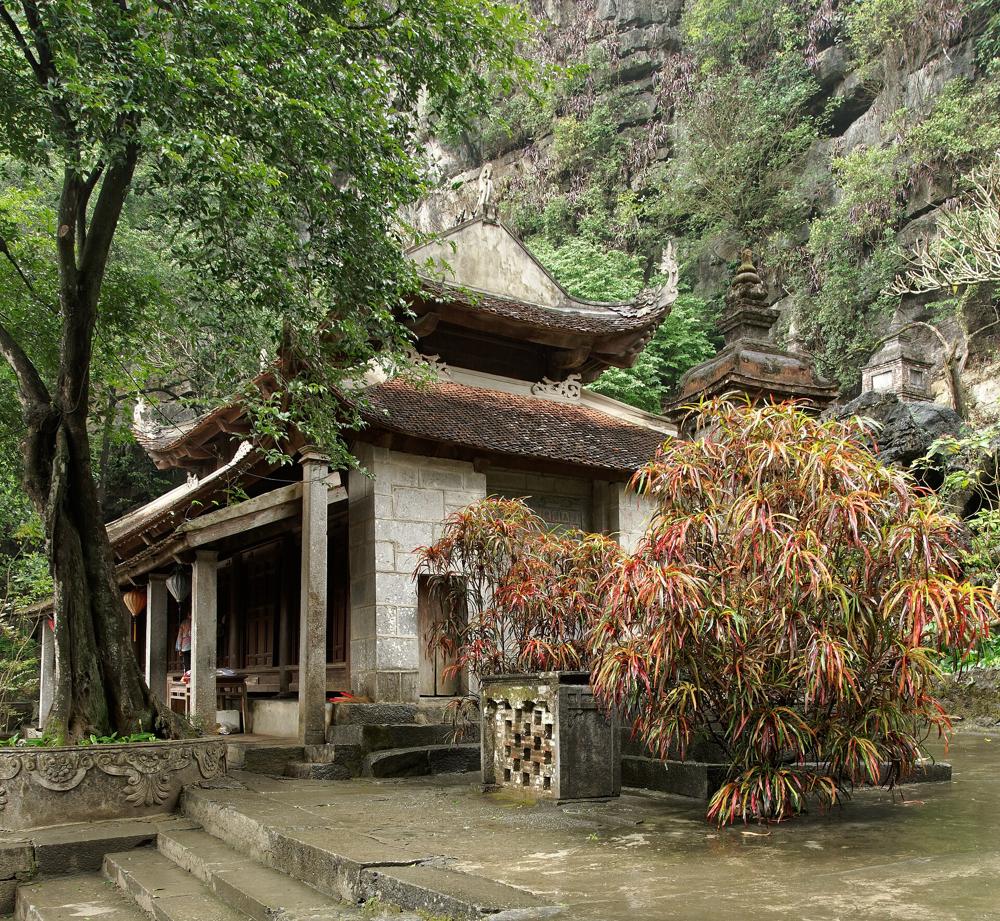 A tiled pagoda hall among trees at the foot of a limestone cliff at Bích Động